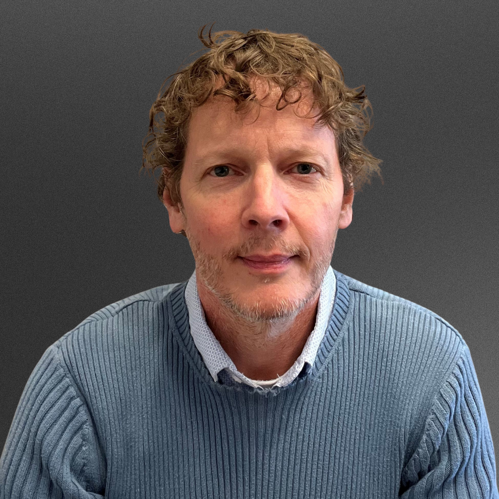 Man with short hair in blue gray sweater with white collared shirt underneath