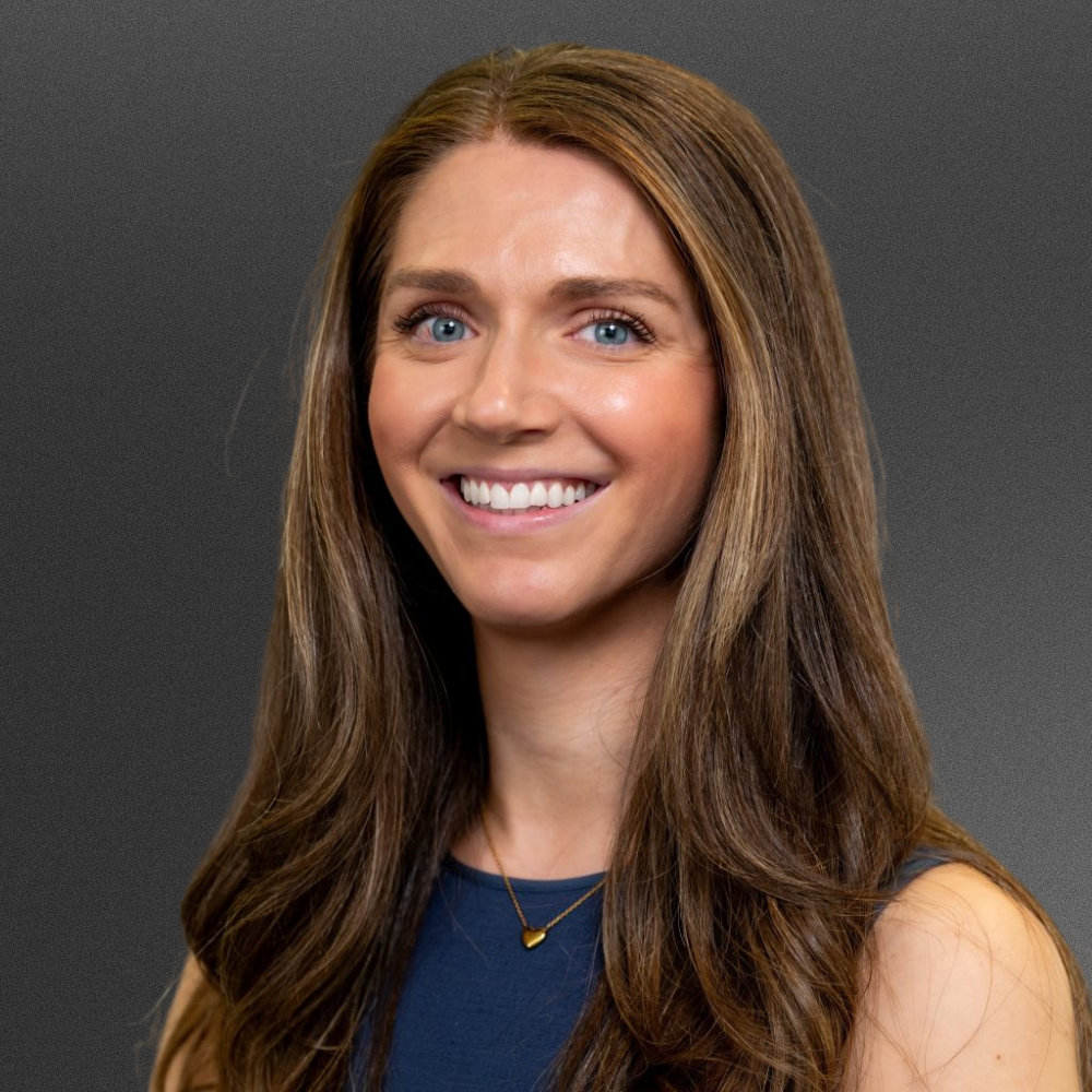 Brunette woman with blue dress and gold necklace.
